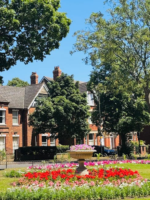 A quiet residential street featuring a row of traditional terraced houses with varying brick facades, some painted in pastel shades, and white window frames. The front gardens are neatly maintained, w